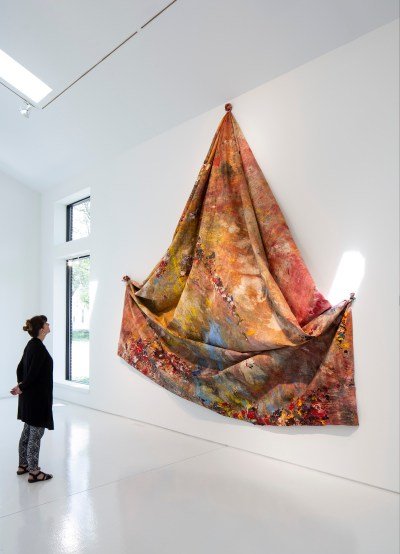 A woman looking at an unstretched abstract painting knotted in three places.
