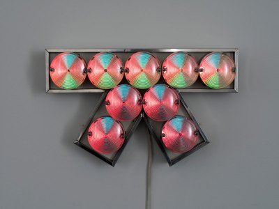 A light sculpture resembling a bow that consists of aluminum, light bulbs, and plastic laminate. 