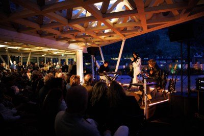 A woman on stage with two bandmates and an audience in front of her.