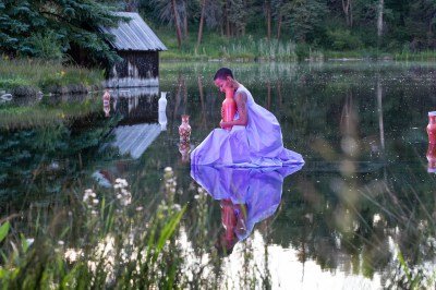 A woman appearing to walk on a lake while holding a ceramic vessel.