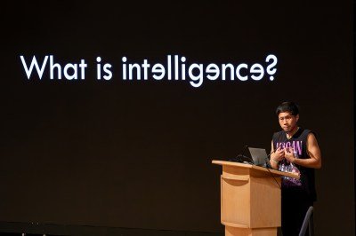 A man at a lectern beneath a projection reading
