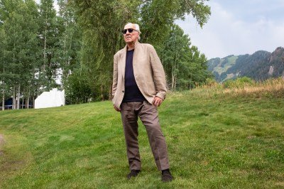 A man standing on green grass in front of a mountainscape.
