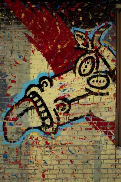 A mural on a brick wall with a cow with its tongue sticking out. 