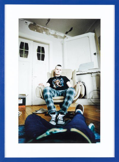 A photograph of a woman sitting in a chair taken by a photographer lying on the floor. The photographer's legs can be seen on the ground.