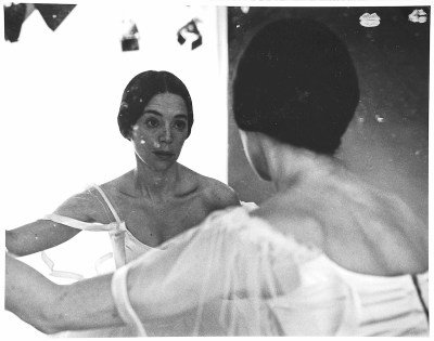 A woman looking at herself in a dirtied mirror.