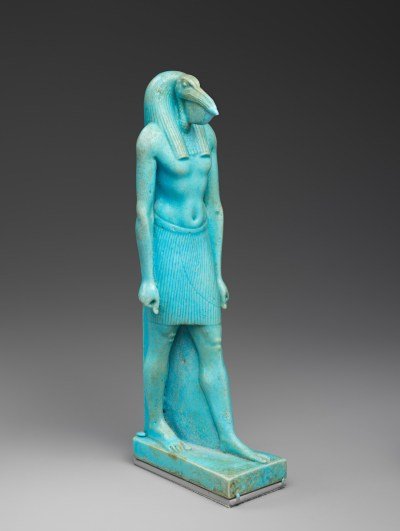 A blue-colored sculpture of a muscular man with a bird's face walking forward.