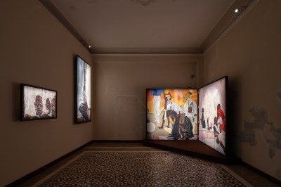 Several paintings showing Black figures in domestic settings in a darkened gallery.