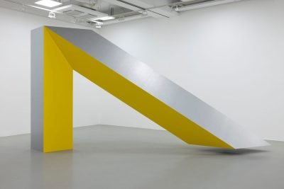 A steel sculpture resembling a large upside down V with one side painted yellow.