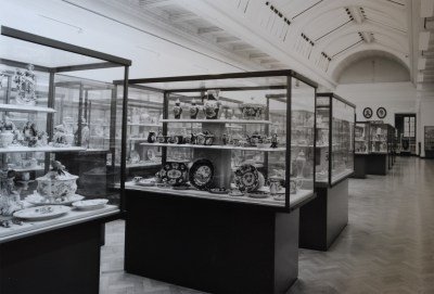An archival photo of a ceramics collection in various vitrines in a museum.