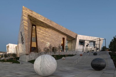View of a museum exterior with a long outdoor stairway on which a sculptural installation of various marble orbs are installed. 