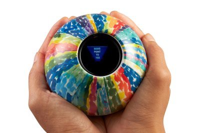 A magic eight ball with an abstract design is held in someone's hands with the message 'signs point to yes' showing. 