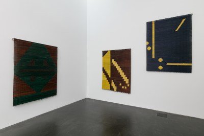 Three mat-like works made from fibers shown on a wall.